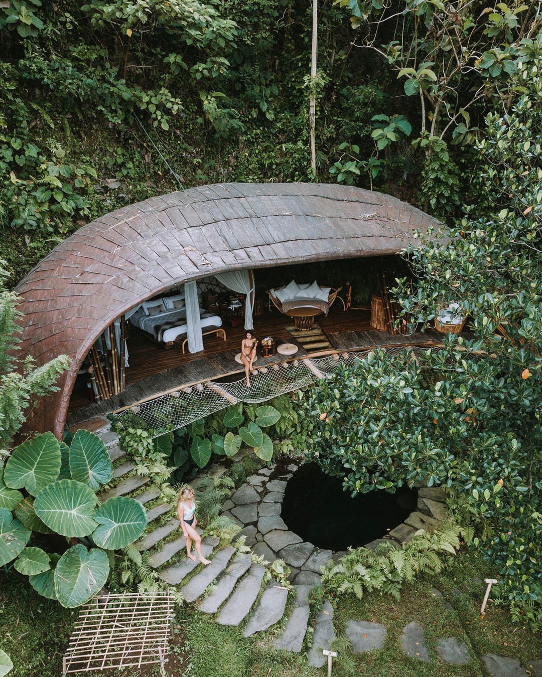 Open bamboo dwelling built into a jungle hillside, deck and stone steps below